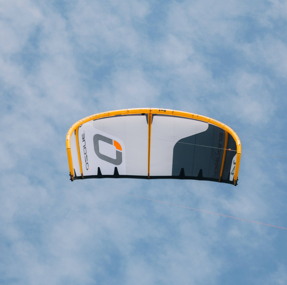 Ozone kite in orange, yellow, and gray flying against a blue sky