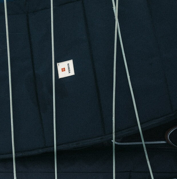 Close-up of a dark navy quilted fabric surface with a small white square label reading MANERA.